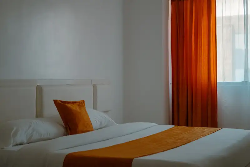 Warm and inviting hotel room with orange curtains and bedding creating a cozy ambiance.