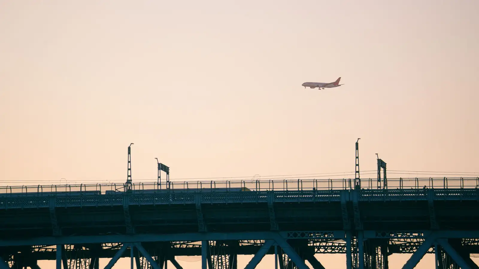 A plane flies over an urban bridge at sunset, creating a stunning silhouette.