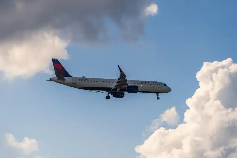 A Delta Air Lines airplane glides through a partly cloudy sky, offering a scenic view.